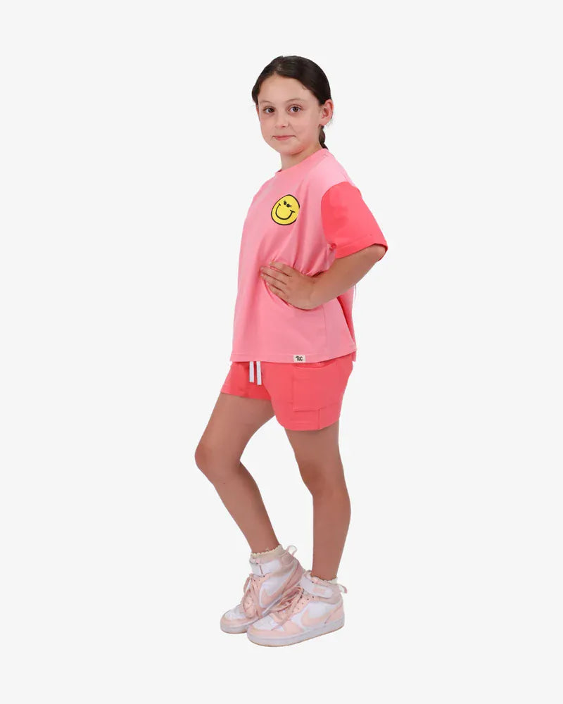 Coral girls' top with happy icon graphics from The Girl Club, featuring a casual and cheerful design perfect for everyday wear.