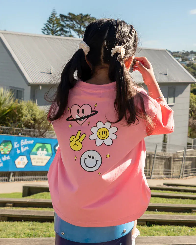 Coral girls' top featuring happy icon graphics from The Girl Club, casual and fun girls' clothing for everyday wear.